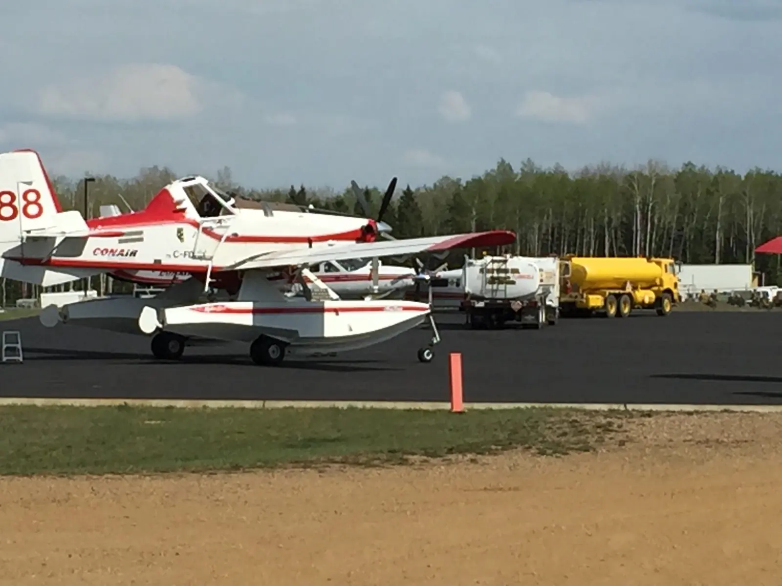A Conair air tanker being fuelled by a Flight Fuels truck on the apron, trees behind