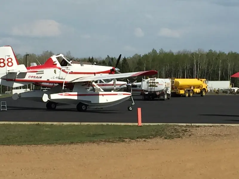 A Conair air tanker being fuelled by a Flight Fuels truck on the apron, trees behind