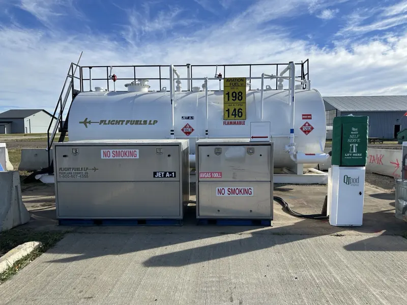 Jet A-1 and avgas skid tanks with placards and a dispensing cabinet at an airfield