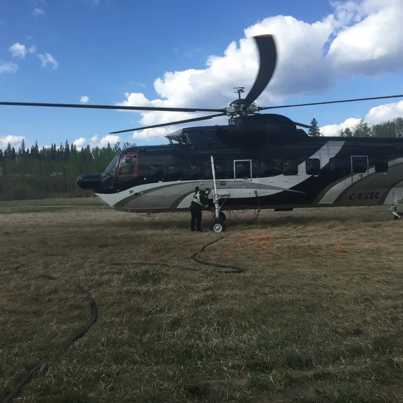 A heavy-lift helicopter being fuelled from a hose on a grass field with crew standing by