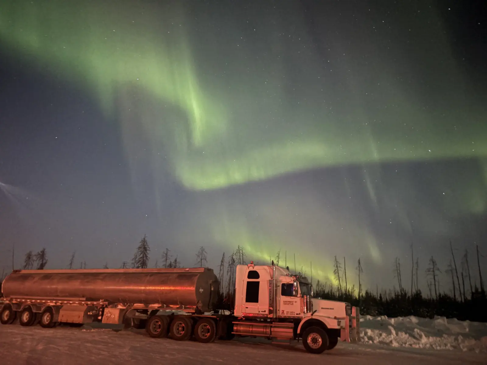 A Flight Fuels tanker truck parked on snow at night under green northern lights
