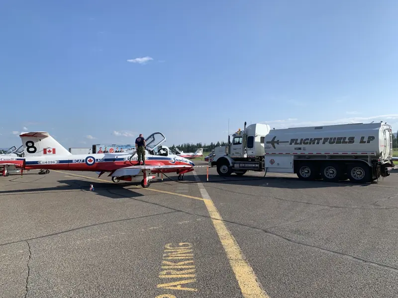 A Flight Fuels tanker truck parked beside a red and white Snowbirds jet on the apron